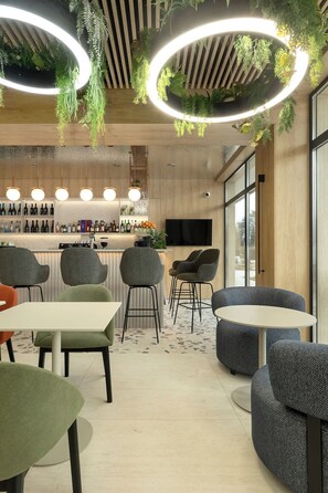 A modern bar area with a wooden bar counter, seating with round tables and chairs, and hanging plants. - Essense Baltic Resort & SPA (Dziwnów)