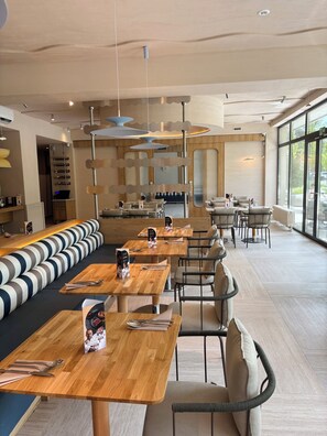 A modern restaurant interior with wooden tables, cushioned seating, pendant lighting, and large windows. - Essense Baltic Resort & SPA (Dziwnów)
