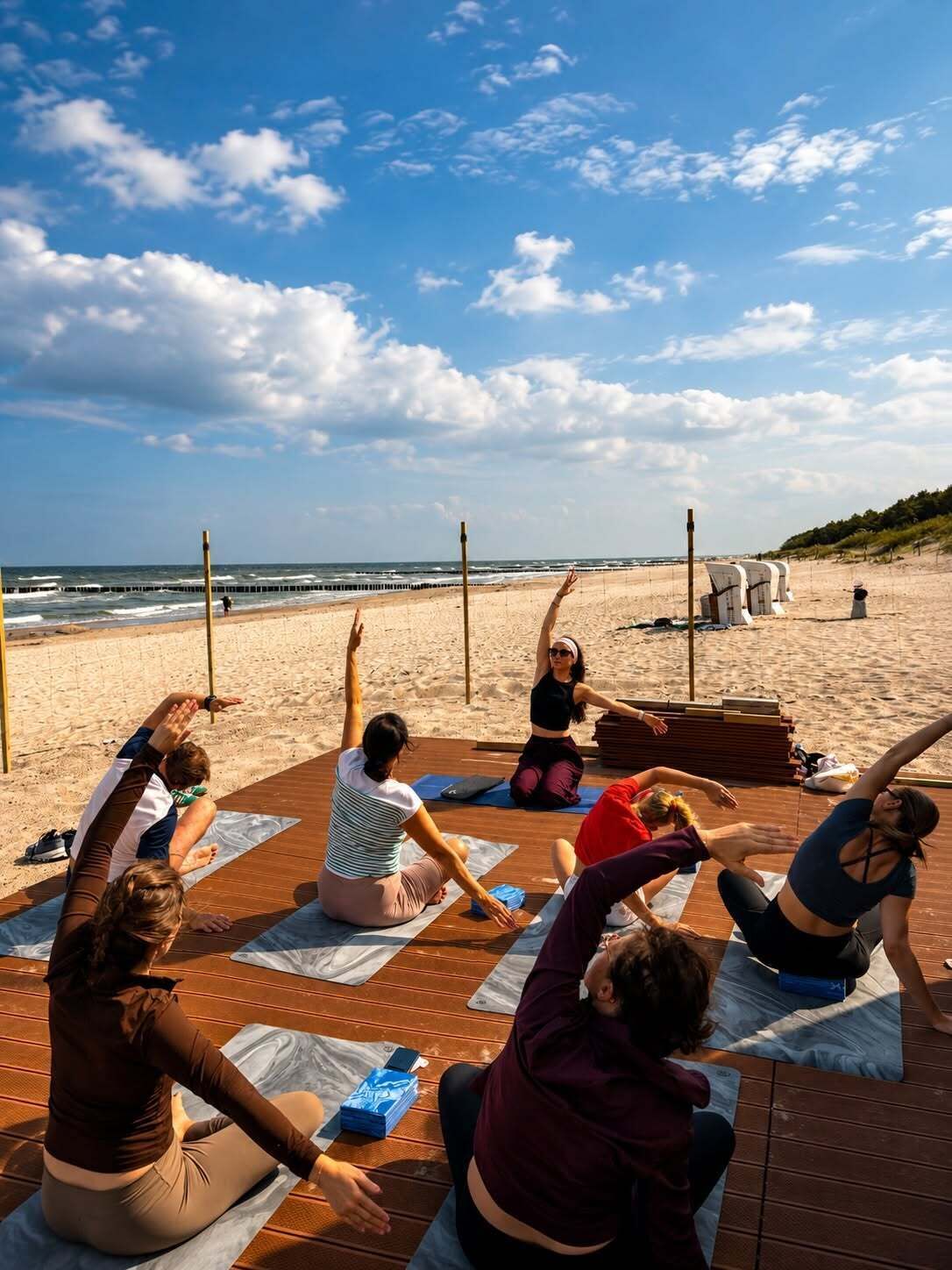 A group of people practicing yoga on mats on a wooden deck by the beach.