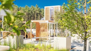 Un espacio exterior moderno con una pérgola de madera, asientos y una fuente de agua.