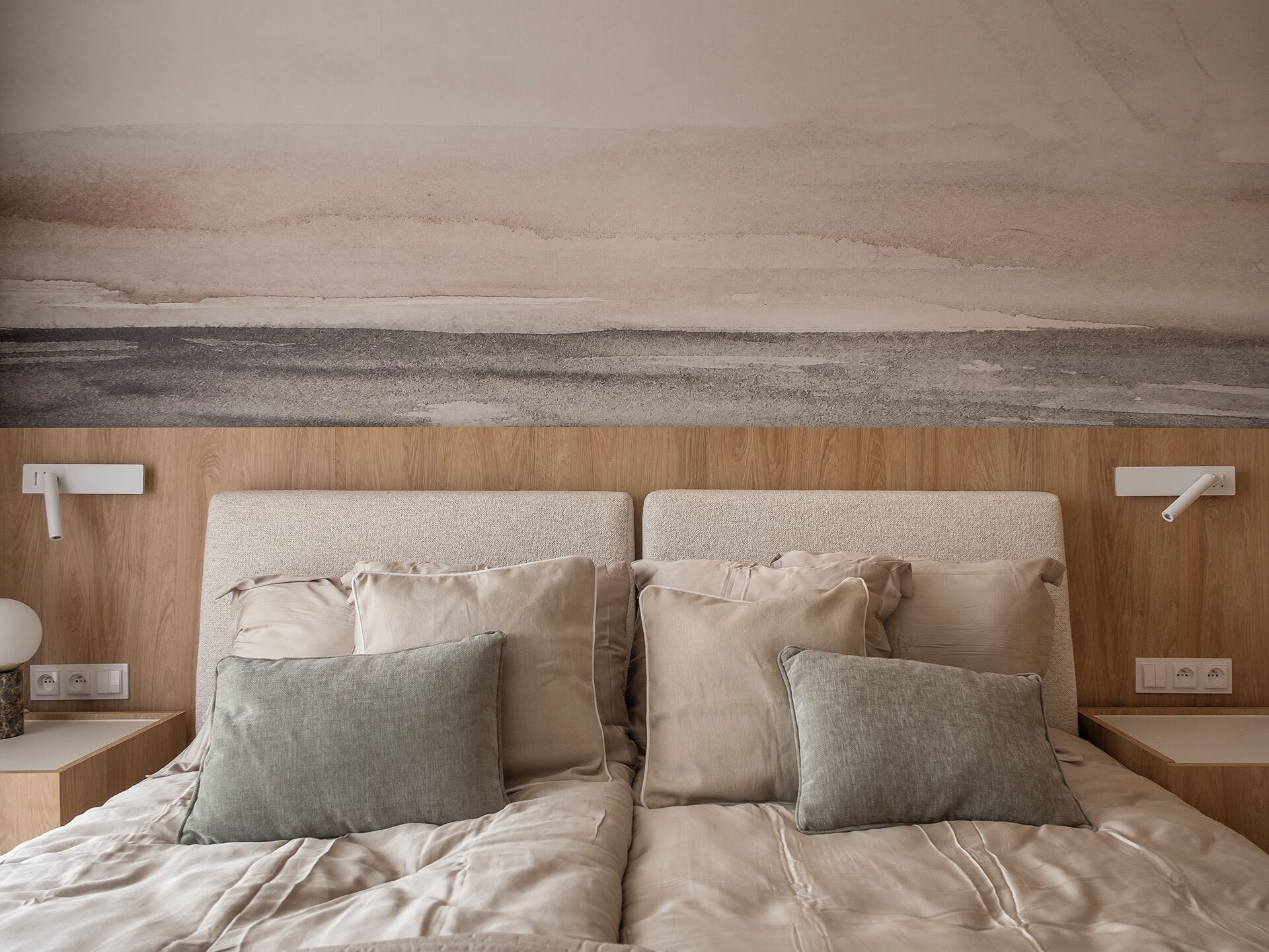 A bedroom with a bed, pillows, a nightstand, and a wall-mounted light fixture.
