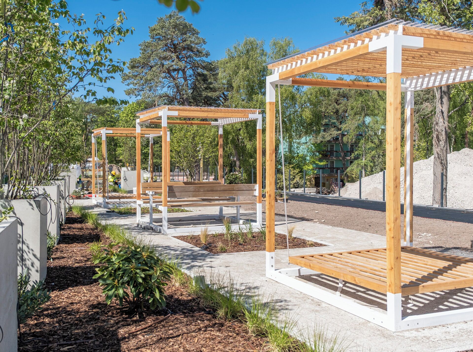 A series of wooden pergolas with benches in a landscaped garden area.