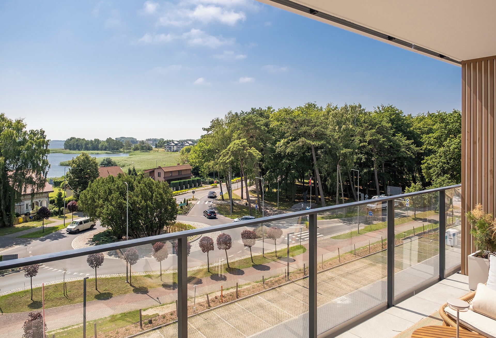 A balcony with a view of a road, trees, and a body of water.