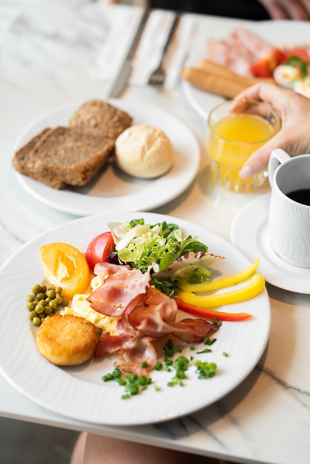A breakfast setting with toast, eggs, bacon, and vegetables on a plate, a glass of orange juice, and a cup of coffee.