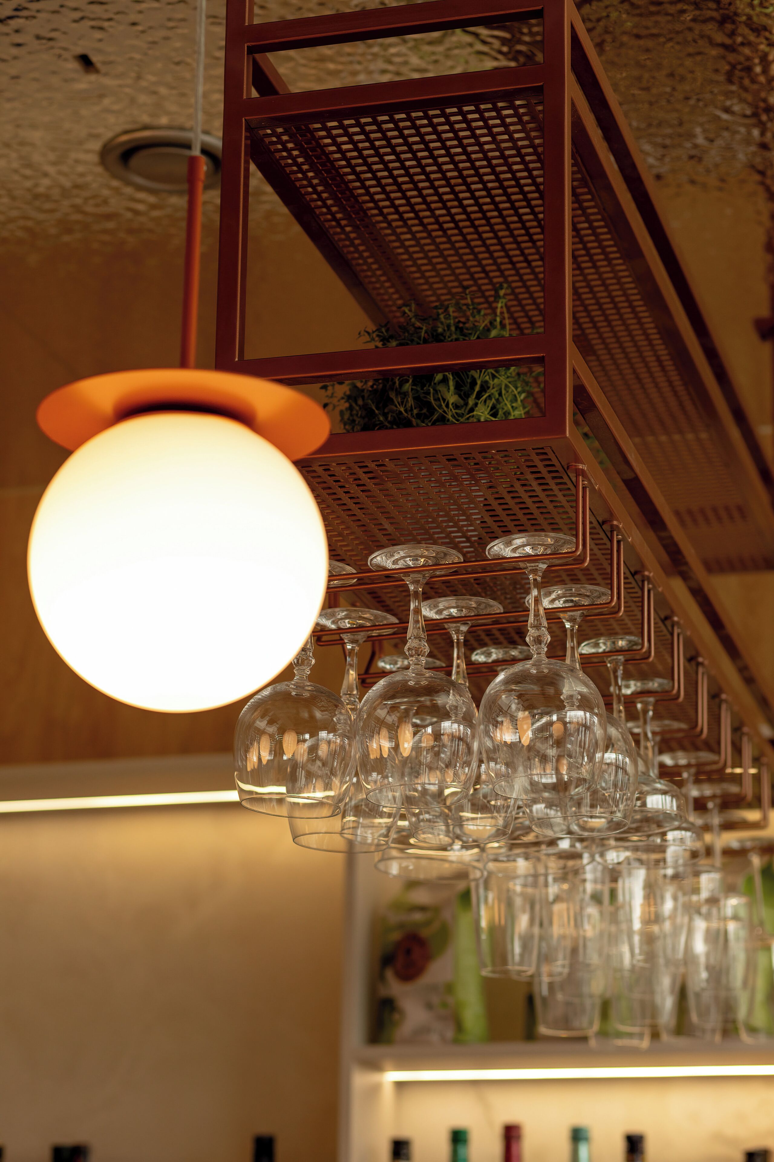 Een plafond met een bolvormige lamp en een metalen rek met daarop verschillende wijnglazen.