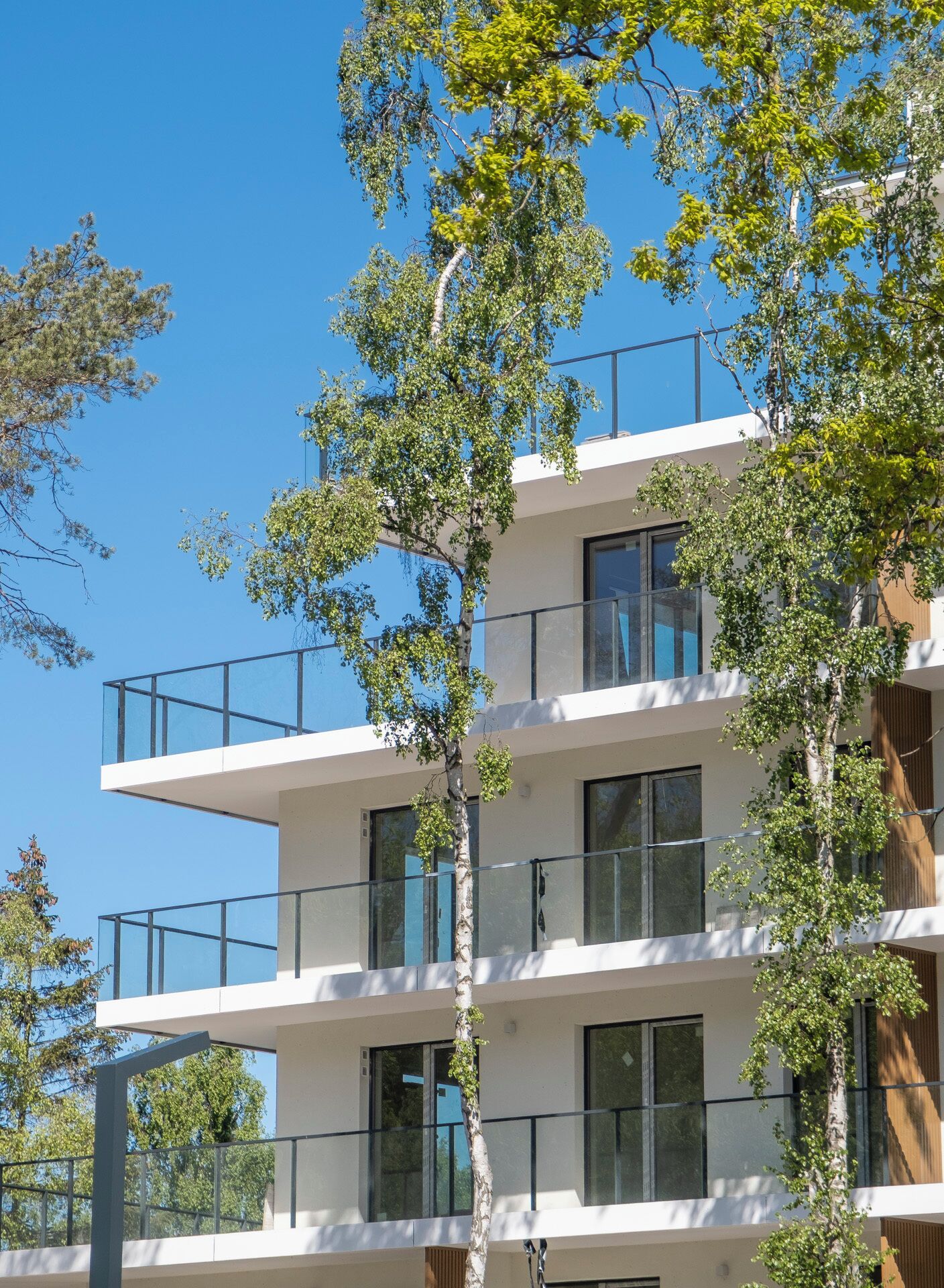 A multi-story building with balconies, large windows, and trees in front.