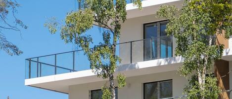 A multi-story building with balconies, large windows, and trees in front.