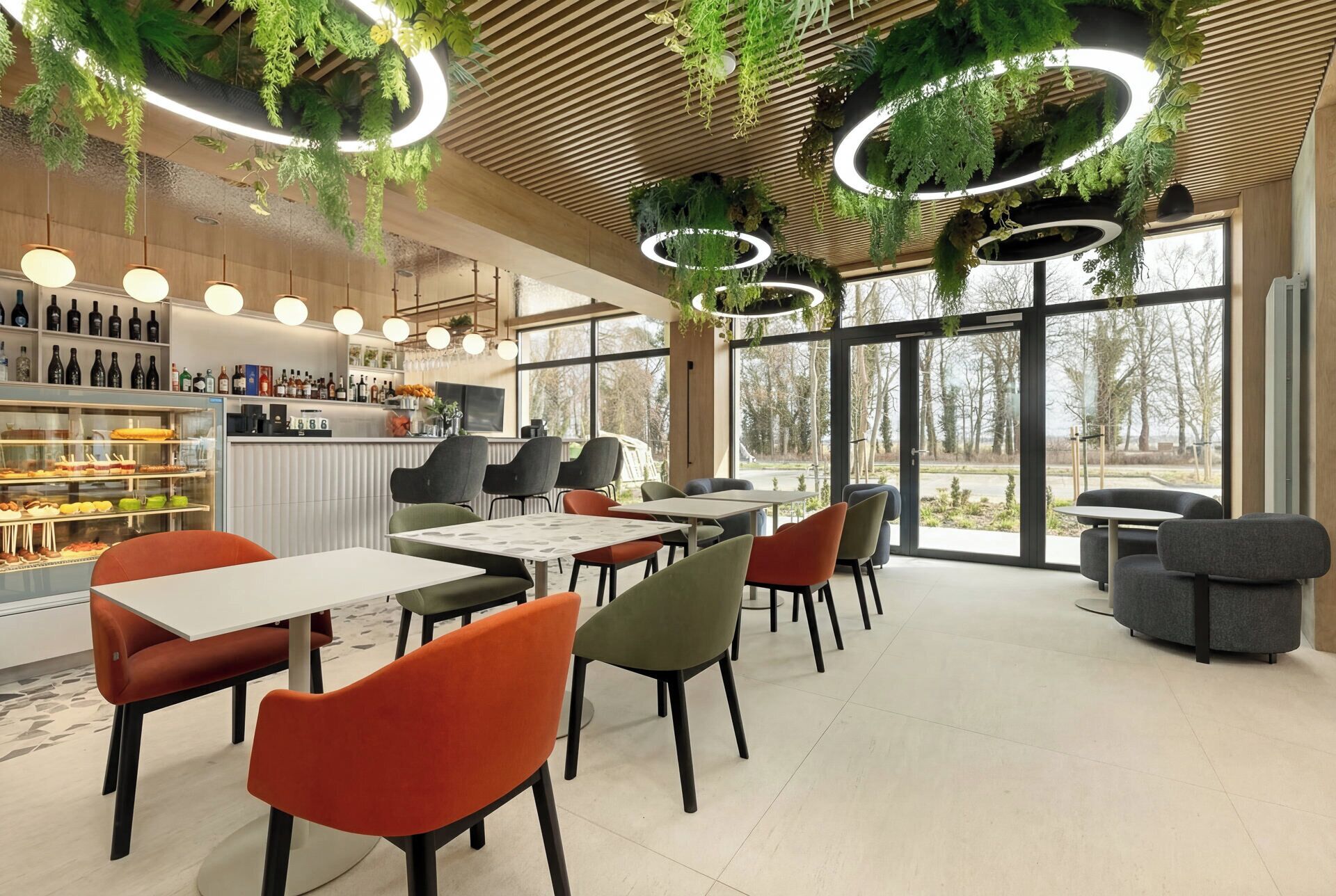 A modern restaurant interior with round tables, chairs, hanging plants, and a bar area with wine bottles.