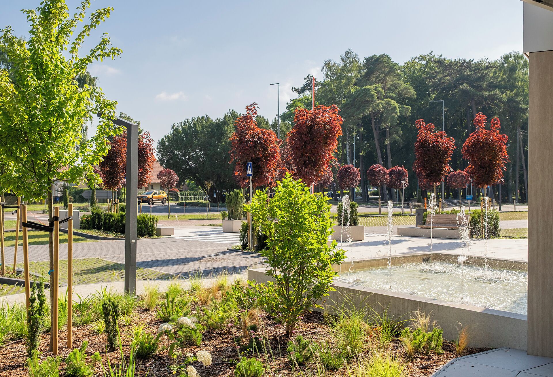 A landscaped area with a fountain, trees, and a pedestrian pathway.