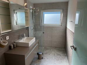 Ein modernes Badezimmer mit großem Spiegel, Waschbecken, Dusche und Fenster.
