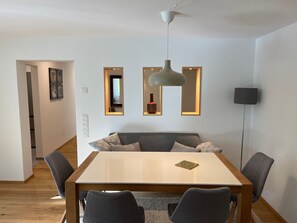 Moderni ruokailutila, jossa on puinen pöytä, harmaat tuolit, harmaa sohva ja kattotuuletin.