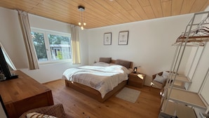 A bedroom with a wooden bed, a desk, a wicker chair, a bedside table with a lamp, and a window with curtains. - Modern Feel-Good Apartment in Marbach am Neckar Near Schillerhöhe (Marbach am Neckar)