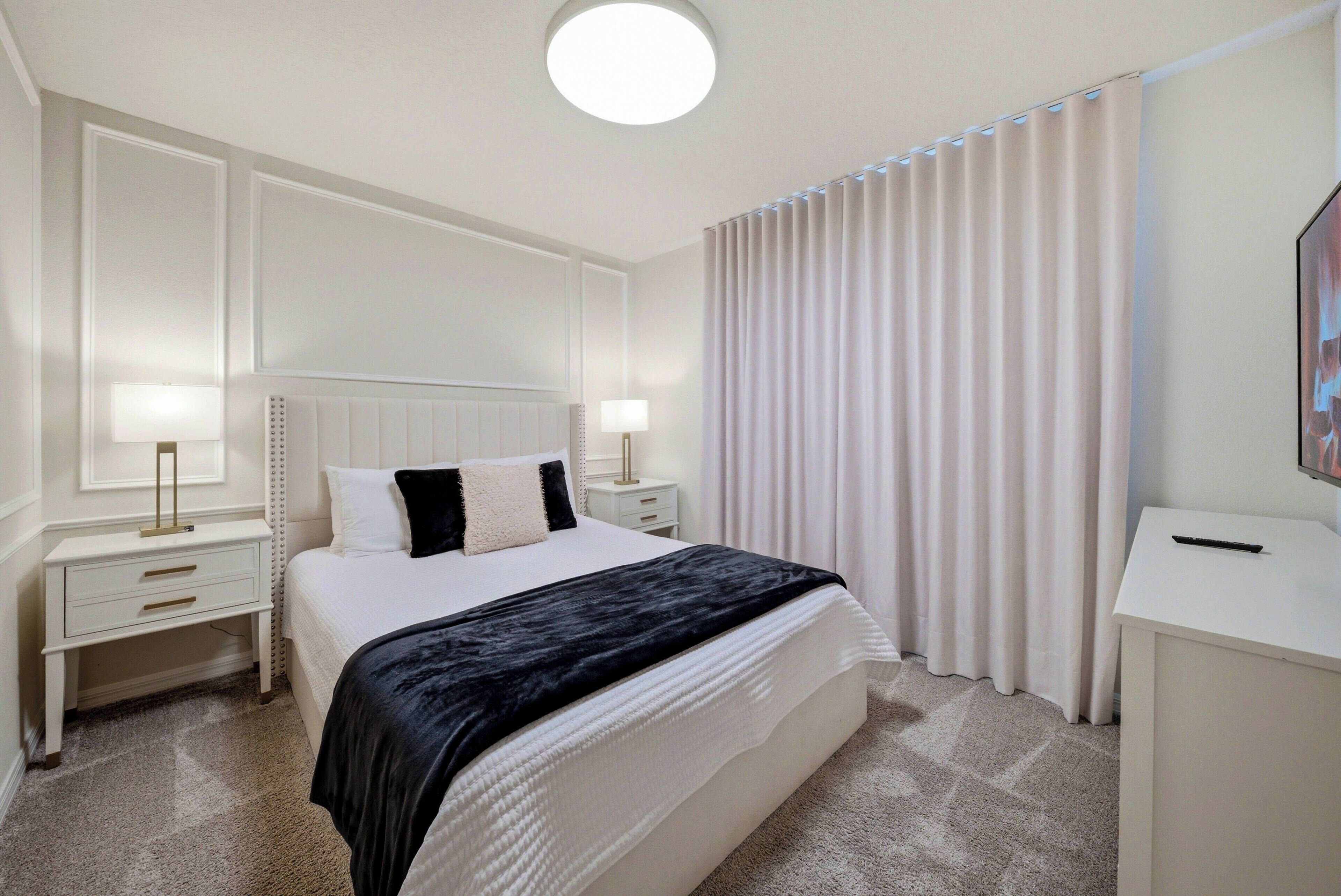 Enjoy restful nights in this beautifully designed bedroom, featuring a plush bed with crisp white linens and elegant black accents. Soft, neutral tones and natural light from the window treatments create a calming atmosphere.
