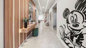 En gang med væg i træpaneler, en grøn skraldespand, en træbænk med krukker og planter, samt et stort muralmaleri af en tegneseriefigur.