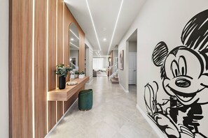 Ein Korridor mit einer Holzwandverkleidung, einer grünen Mülltonne, einer Holzbank mit Blumentöpfen und einem großen Wandgemälde eines Comic-Charakters.