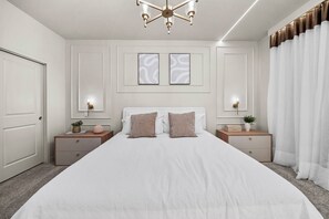 Ein Schlafzimmer mit einem großen Bett, zwei Nachttischen, einer Chandelüstere und einer Tür.