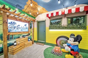 Ein Kinderspielbereich mit einem großen Fernsehbildschirm, Holzspielgeräten und einer Mickey Mouse Statue.