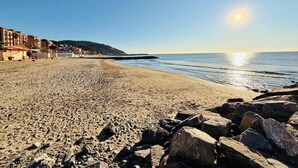 A beach with a rocky shoreline, buildings in the background, and a clear sky. - Attico del Sole con Vista Mare e Terrazza (Marina di Andora)