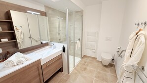 Une salle de bain moderne avec une douche à parois de verre, un grand miroir, un lavabo blanc et des toilettes.