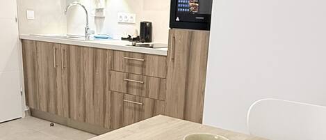 Una cocina moderna con armarios de madera, microondas integrado y una mesa de comedor blanca con dos sillas.