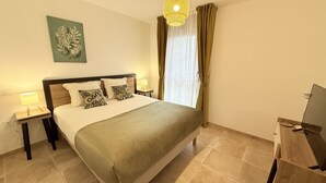 Une chambre à coucher bien rangée, avec un lit, deux tables de chevet, une lampe, un téléviseur et une fenêtre avec des rideaux.