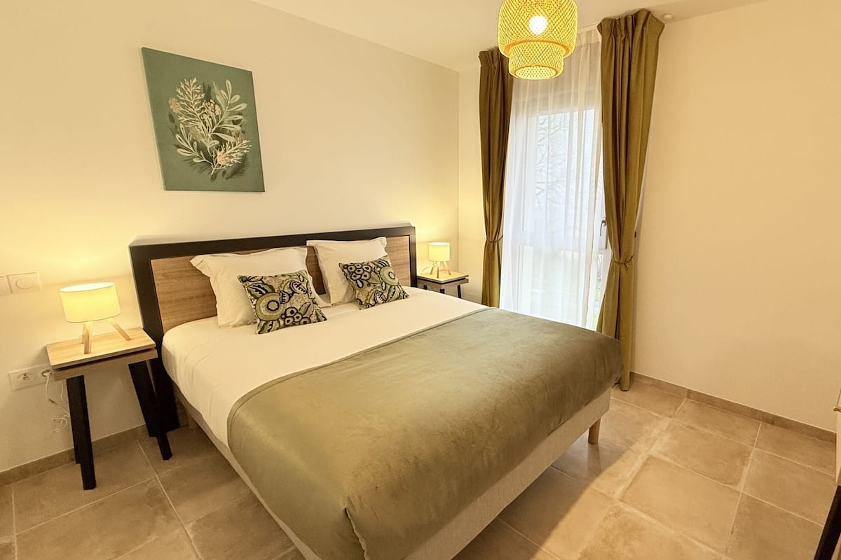 Une chambre à coucher bien rangée, avec un lit, deux tables de chevet, une lampe, un téléviseur et une fenêtre avec des rideaux.