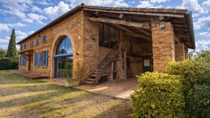 A rustic brick building with a large arched entrance, a staircase leading to an upper level, and a small garden area with a potted plant and bushes. - Charming renovated farmhouse with river and forest area (Orgueil)