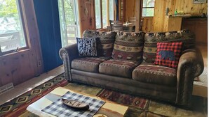 A cozy cabin interior with a leather sofa, patterned cushions, and a checkered tablecloth. - Cozy 2 bedroom cottage on lake! (Mountain)
