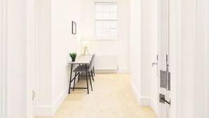 A narrow hallway with a dining area at the end, featuring a table with chairs, a small plant, and a lamp. - *NEW* Artisan Apartment | Modern | Spacious (Gloucestershire)