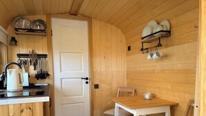 Eine kleine Küche mit weißer Tür, Holzvertäfelung, einem Esszimmertisch mit Stühlen und einer Kaffeestation.