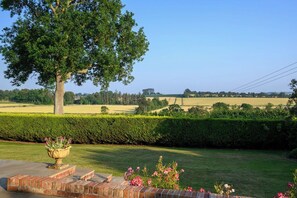 Un jardín arbolado con un gran árbol, un camino de ladrillo y vistas al campo.