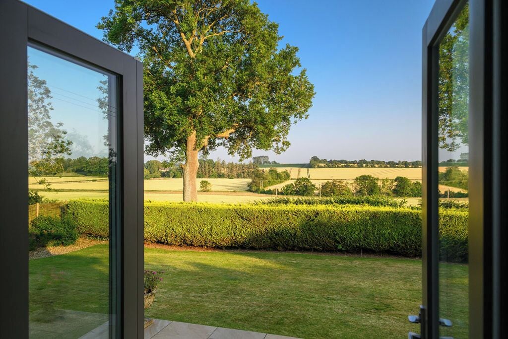 A view from a room with large windows overlooking a well-maintained garden with a prominent tree and neatly trimmed hedges.