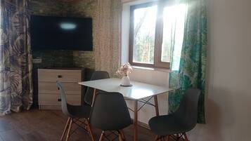 Un coin repas avec une table et des chaises, un téléviseur à écran plat fixé au mur et une fenêtre avec des rideaux.