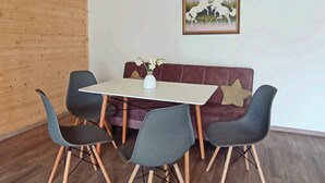 A dining area with a wooden ceiling, a white table, and four chairs. A sofa with cushions is against the wall, and a framed picture hangs above it. - Amrakits Canyon Guesthouse (Amrakits)