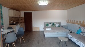 A room with a bed, a sofa, a small table, a chair, a kitchenette, and a wooden ceiling. - Amrakits Canyon Guesthouse (Amrakits)