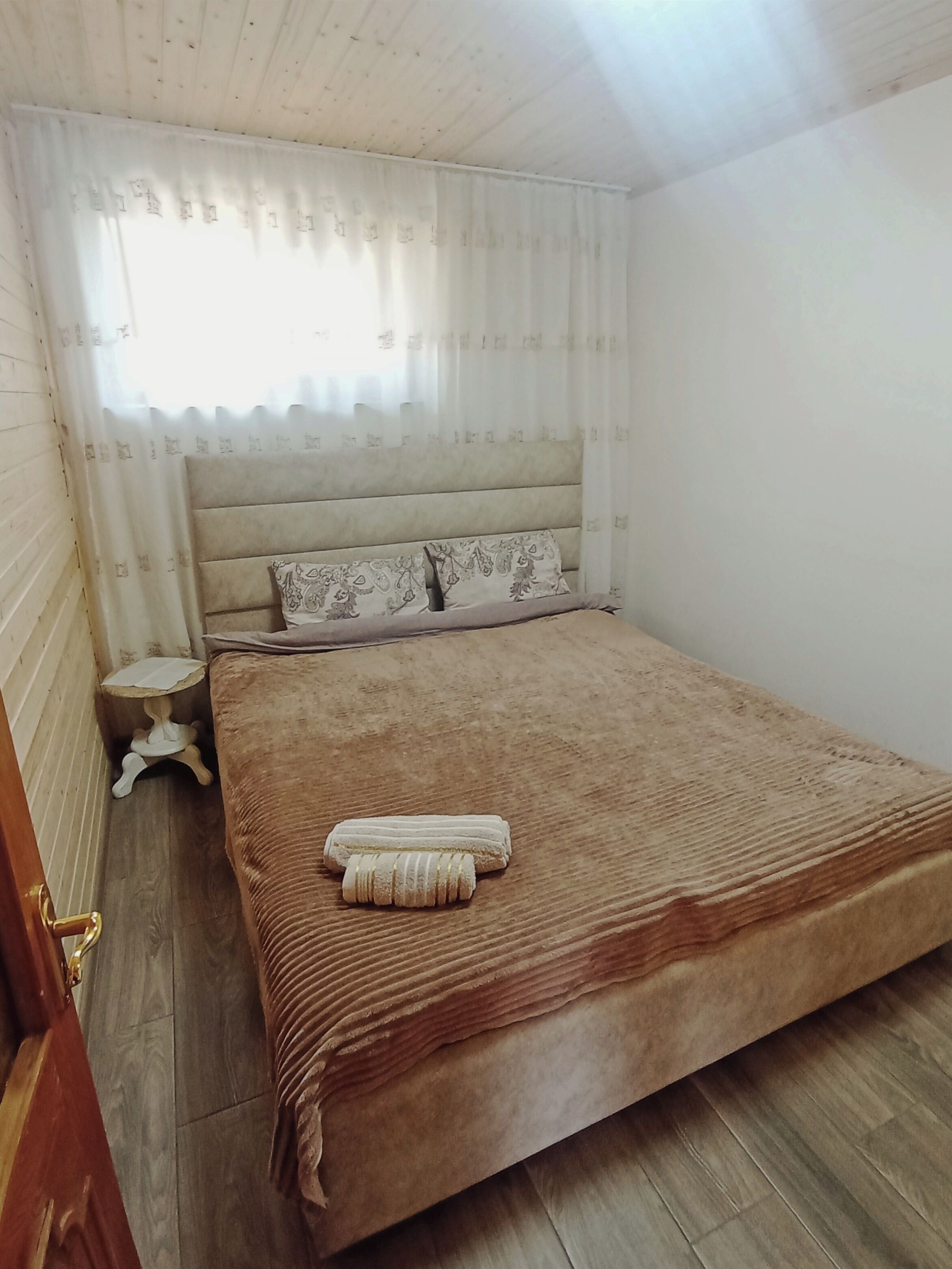 Een slaapkamer met een groot bed, een nachtkastje en een raam met dunne gordijnen.