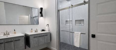 A modern bathroom with two sinks, a large mirror, and a glass-enclosed shower area.