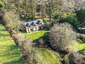 A stone house with a sloped roof and multiple windows, surrounded by a well-maintained lawn and dense shrubbery. - Pandia Cottage, Warleggan - Idyllic Surroundings - Sleeps 5 + dogs + parking (Cornwall)