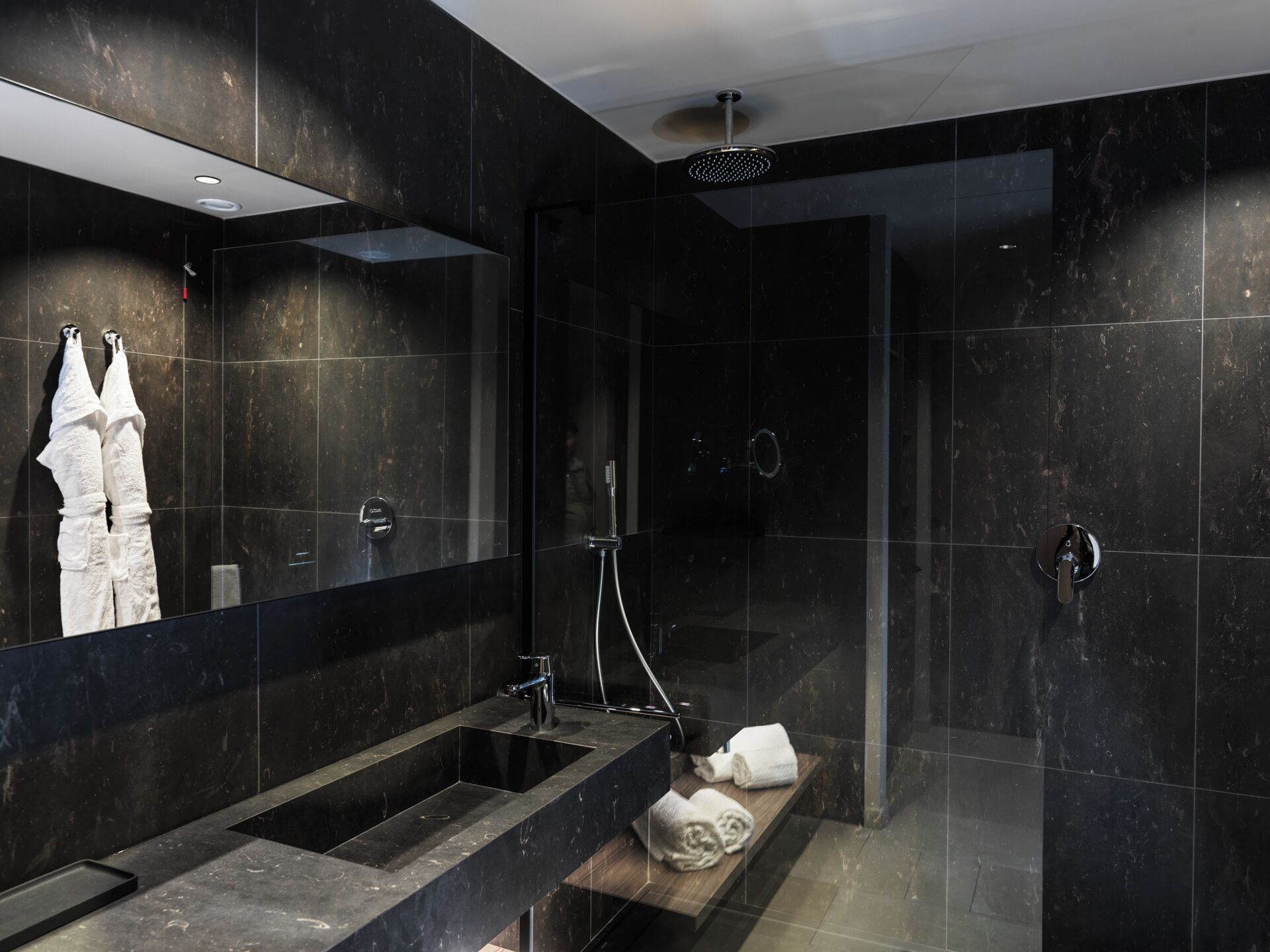 A modern bathroom with a large mirror, a sink, a shower, and a towel rack.