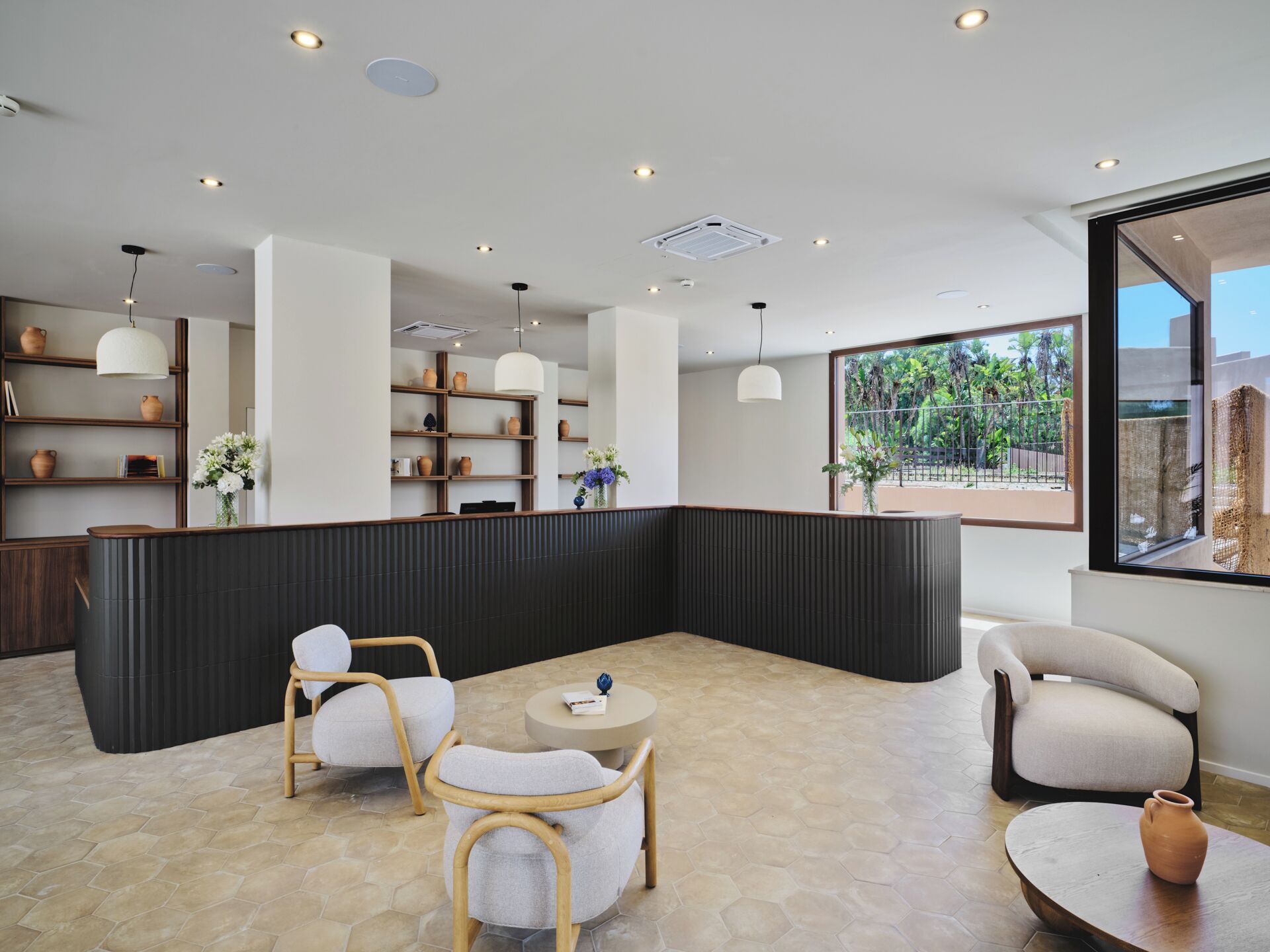 A modern interior with a seating area, shelves with pottery, and a view through a large window.