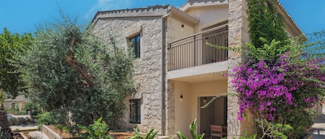 A stone building with a balcony and a garden with various plants and flowers.