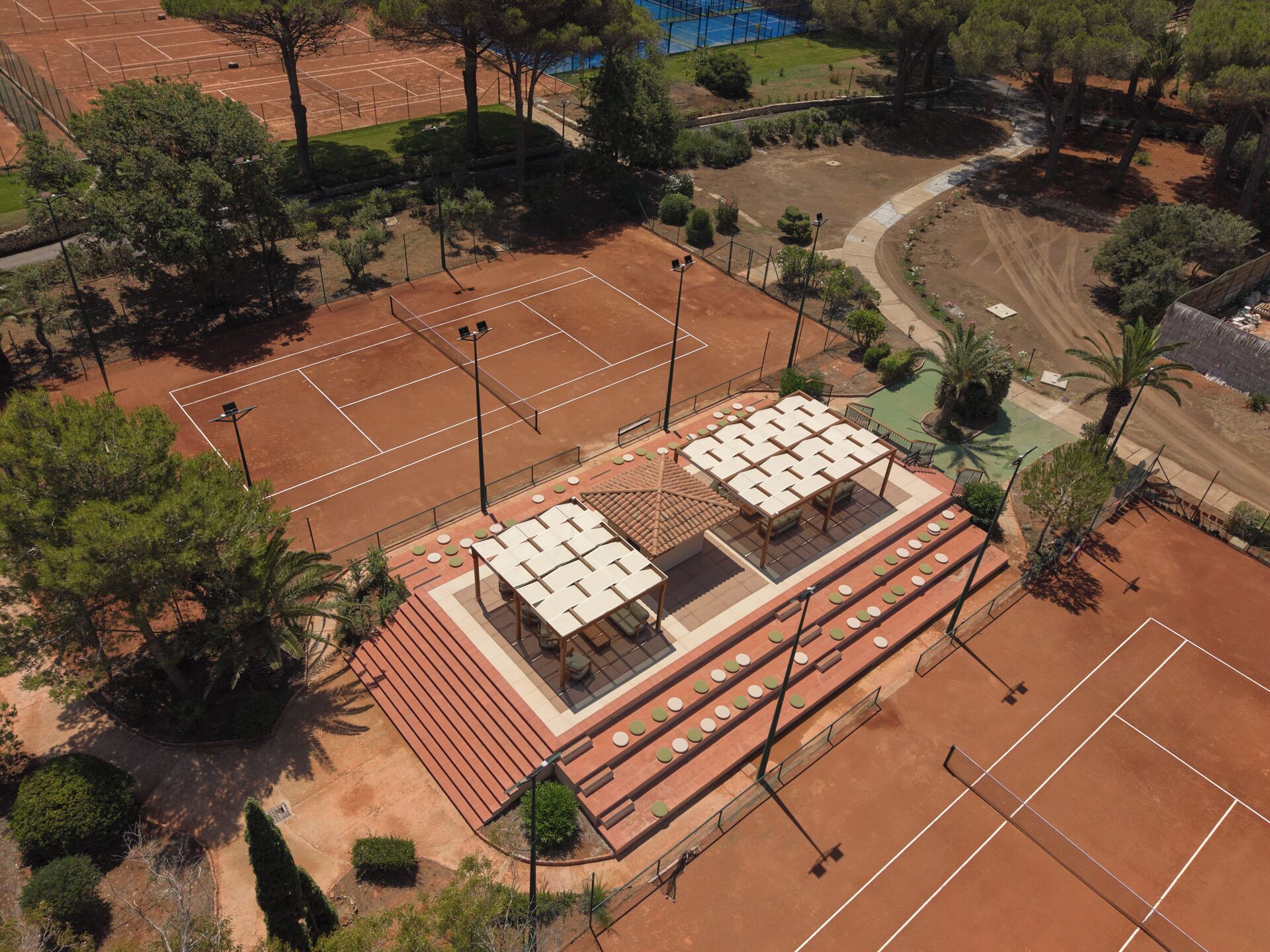 An aerial view of a tennis court complex with multiple courts, seating areas, and surrounding greenery.