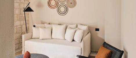 A modern living room with a white sofa, a round black table, a black woven chair, and a decorative wall piece.