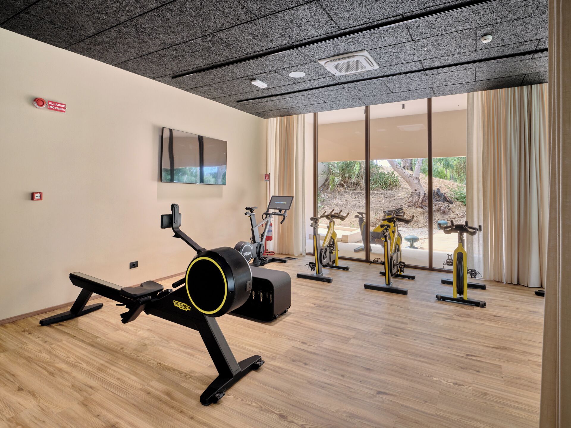 Ein Fitnessraum mit Trainingsgeräten, einem Fernseher und großen Fenstern.