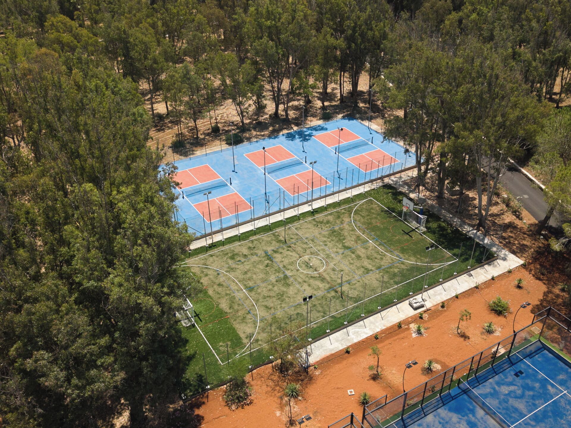 An aerial view of a sports complex with multiple tennis courts, a basketball court, and a swimming pool.