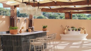 Une cuisine extérieure avec un bar, des chaises en osier et des plantes en pot.