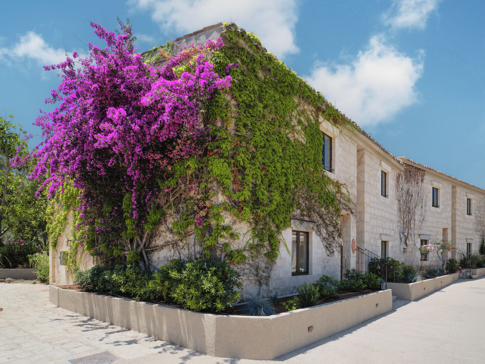 A building with a stone facade, a balcony, and a garden with purple flowers.