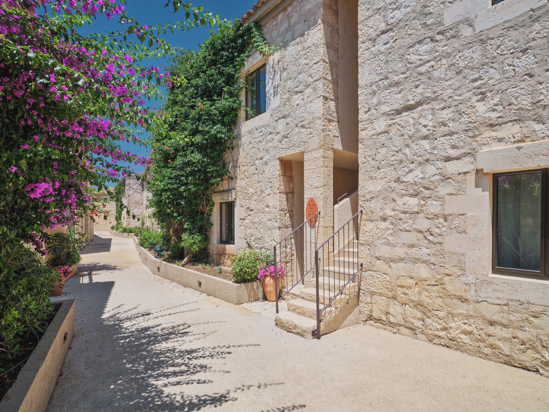 A narrow street with stone buildings, a staircase, and flowering plants.