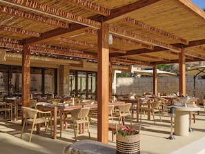 An outdoor dining area with wooden tables and chairs, stone walls, and a pergola structure. - Mangia's Costa Ragusa Borgo - New Opening (Scoglitti)