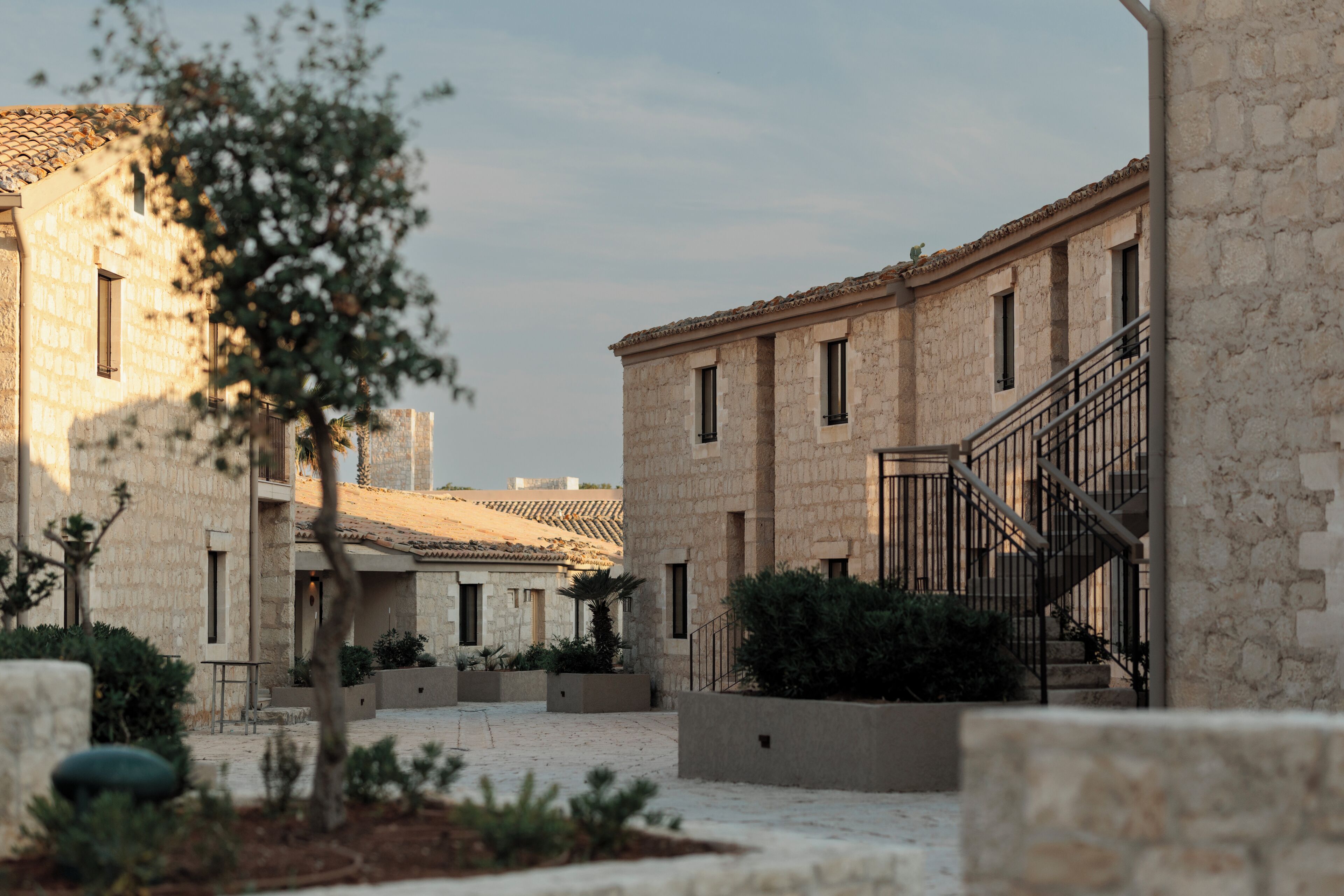 A courtyard with stone buildings, a staircase, and some greenery.